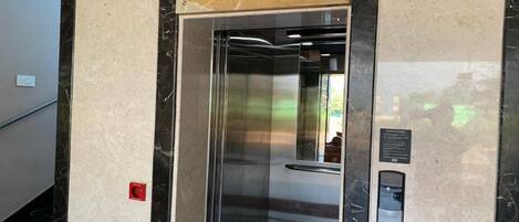 Un ascensore con interni metallici, un pulsante rosso di emergenza e un pannello di controllo con frecce direzionali.