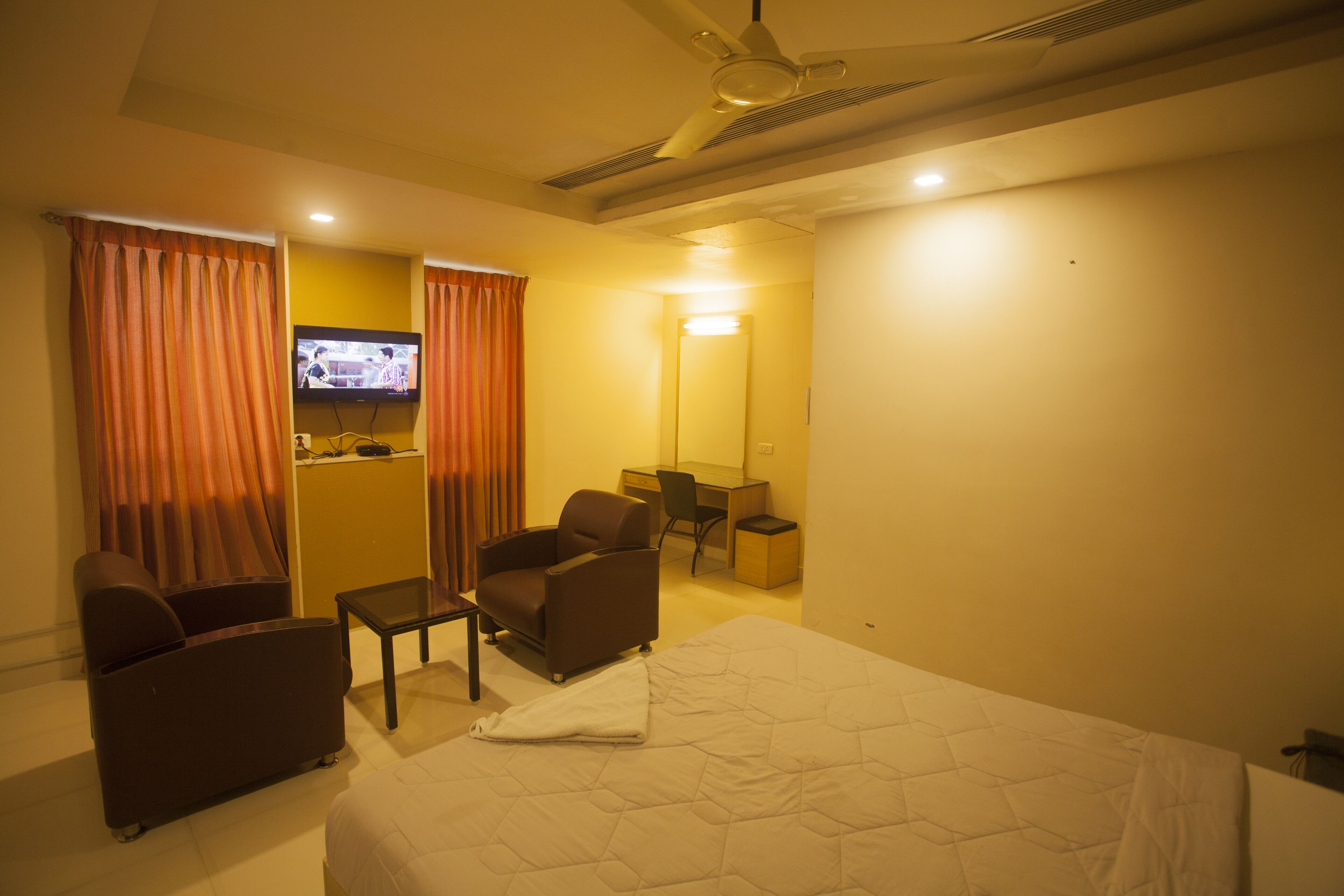 Habitación de hotel con cama, dos sillones, escritorio, televisor y espejo.