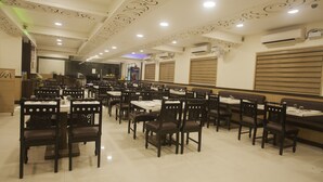 A spacious restaurant with multiple dining tables and chairs, featuring a modern ceiling design and air conditioning units. - Ganesh Meridian (Tiruppattur)