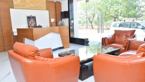 A modern reception area with leather sofas, a marble reception desk, and a large window offering a view of the outside. - Ganesh Meridian (Tiruppattur)