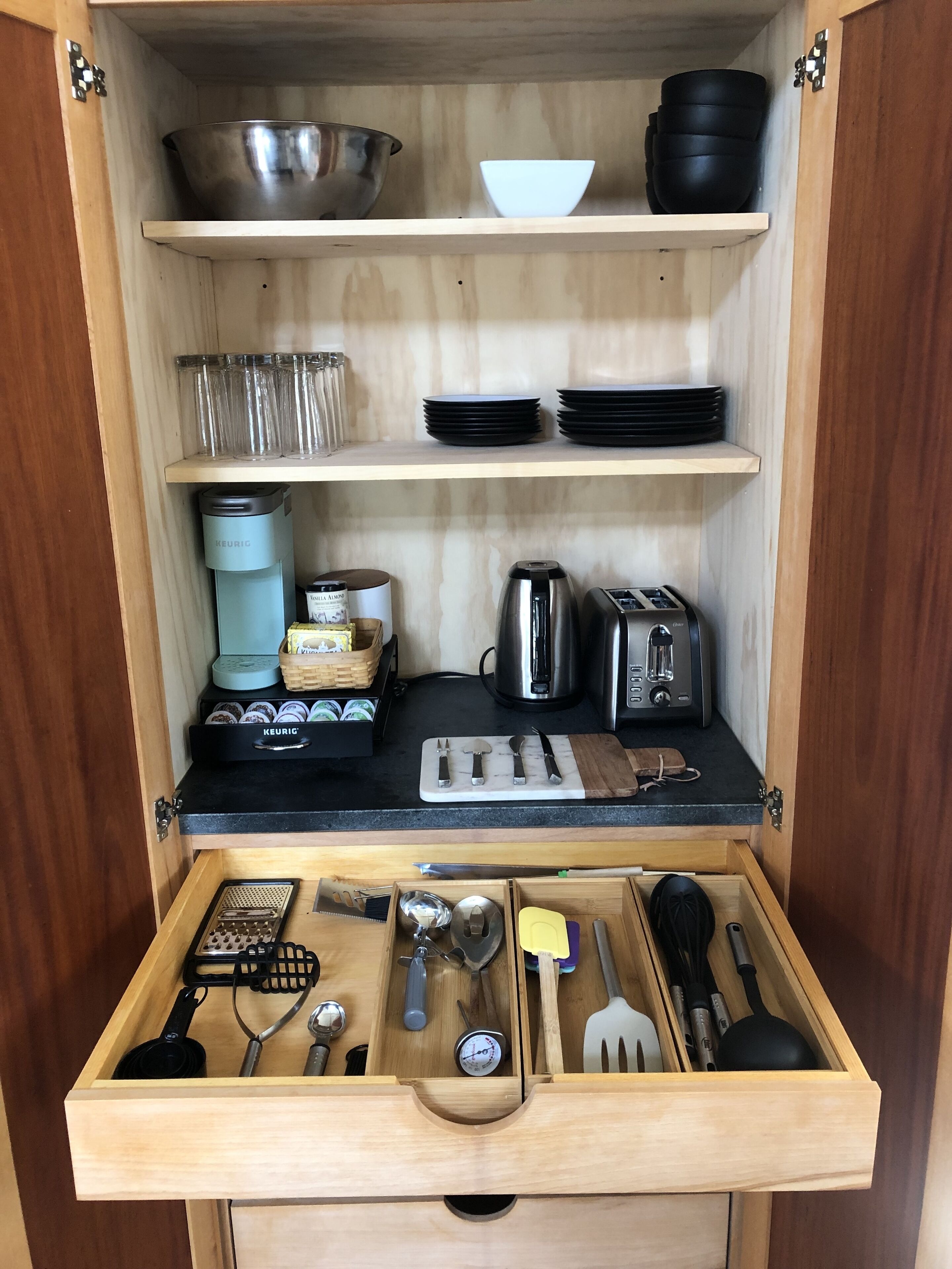 Un mueble de cocina con repisas que sostienen cuencos, platos y una cafetera.