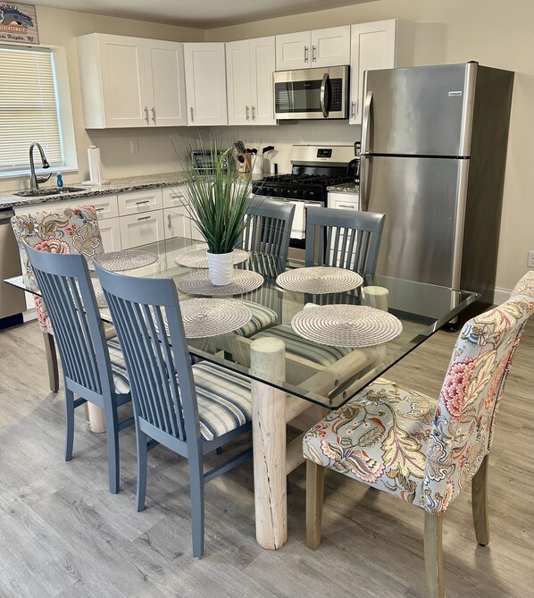 A modern kitchen with white cabinets, stainless steel appliances, and a glass dining table with blue chairs.