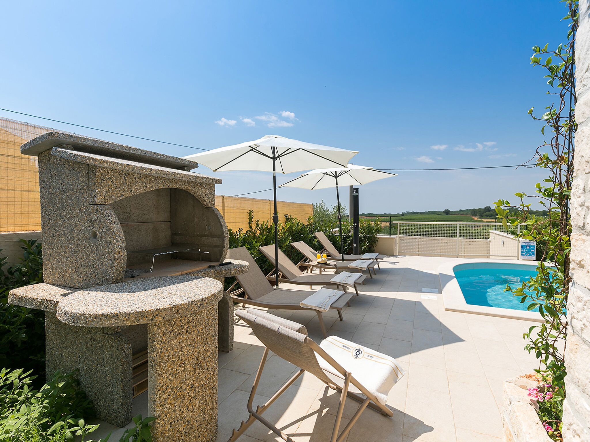 Un área de piscina en la azotea con sillones de descanso, una parrilla y sombrillas.