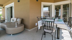 A dining area with a round table and chairs, a cushioned seating area, and large windows.