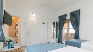 A hotel room with two beds, a TV, a wardrobe, a small table with a vase, and a door leading to a bathroom.