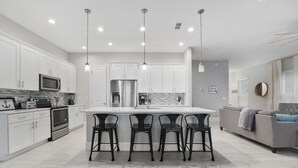 A modern kitchen with white cabinets, stainless steel appliances, and a central island with bar stools. - Gorgeous Waterfront w/ Golf Cart! 4 bds, 3.5 ba! Sleeps 12 (St. Augustine)