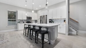 A modern kitchen with white cabinets, stainless steel appliances, and a central island with bar stools. - Gorgeous Waterfront w/ Golf Cart! 4 bds, 3.5 ba! Sleeps 12 (St. Augustine)