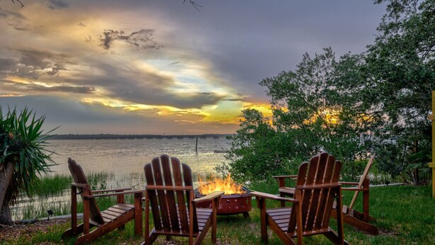 Two Adirondack chairs facing a fire pit with a lake and sunset in the background. - Gorgeous Waterfront w/ Golf Cart! 4 bds, 3.5 ba! Sleeps 12 (St. Augustine)