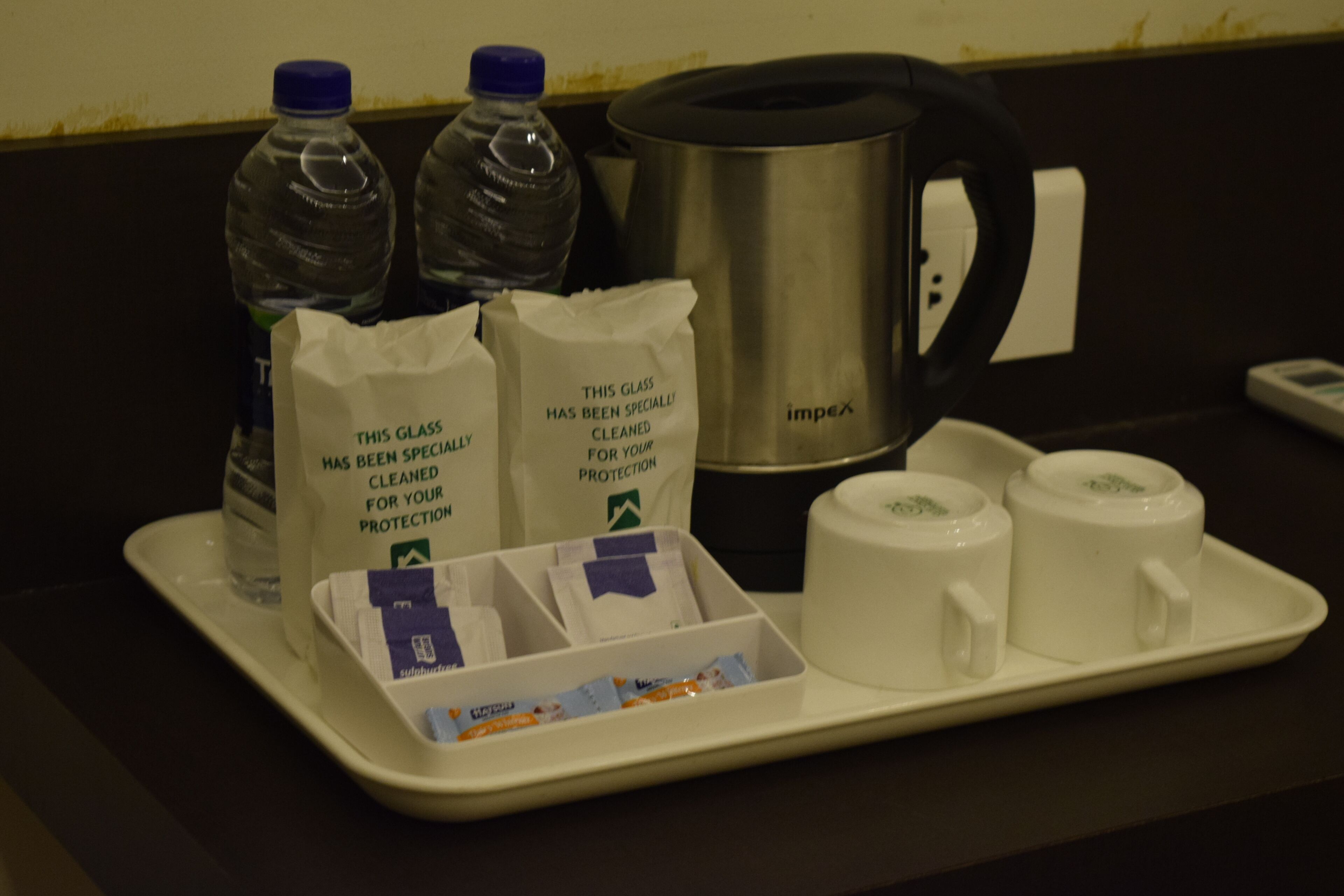 A tray with two water bottles, two coffee cups, a kettle, and two bags of coffee pods.