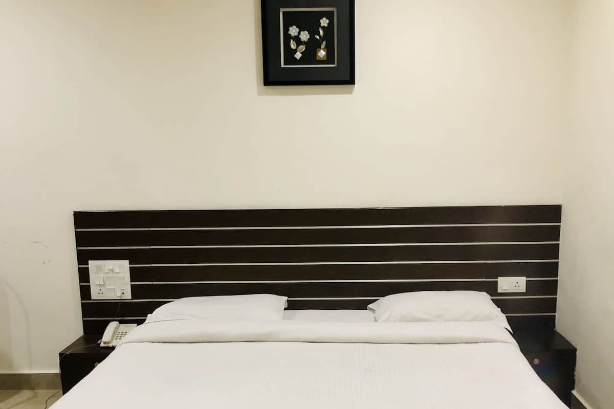 A neatly made bed with white linens, a black headboard, and a framed picture on the wall.