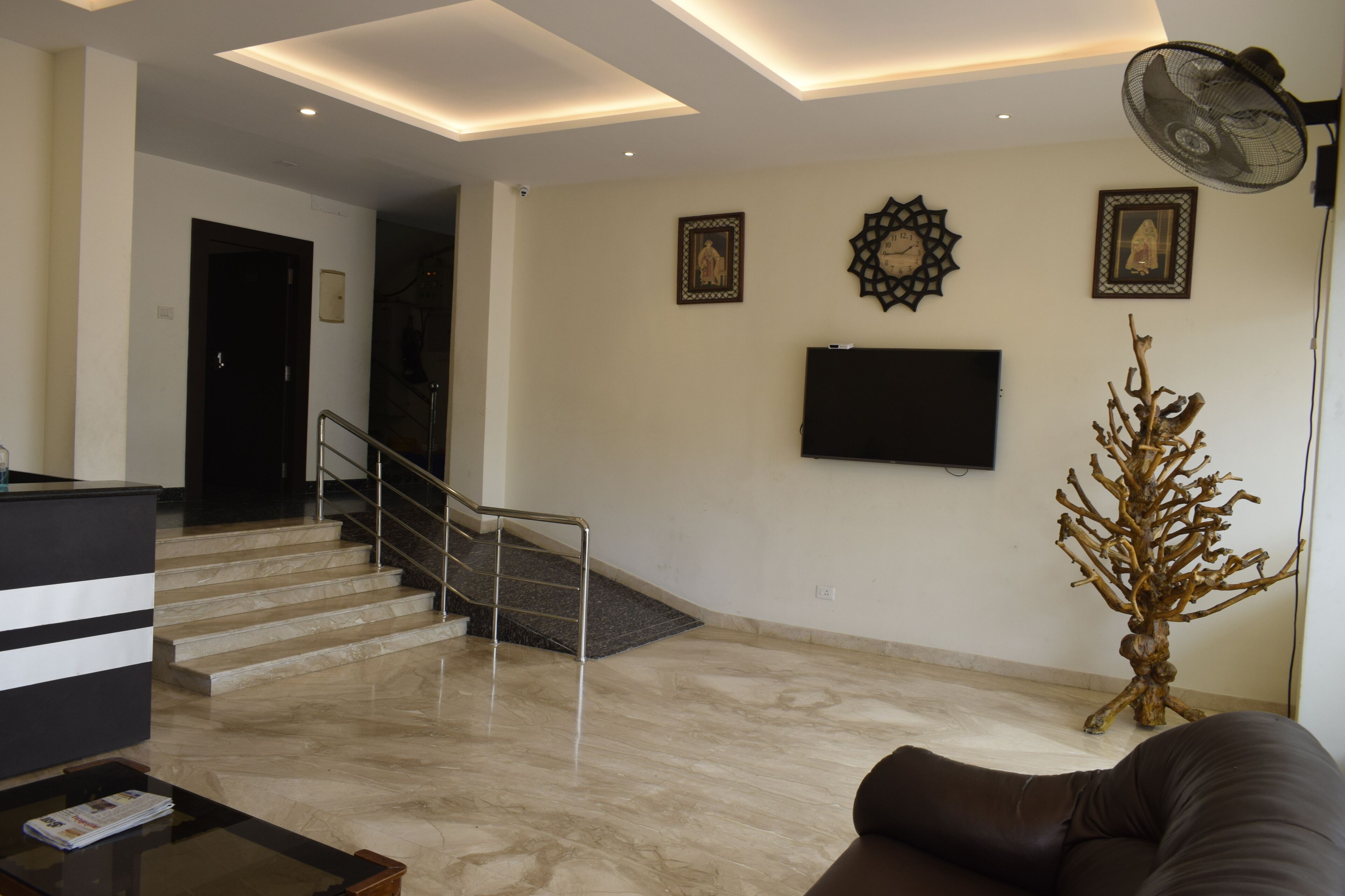 Amplia zona de estar con piso de mármol, una escalera, un televisor de pantalla plana montado en la pared y una escultura de árbol decorativa.