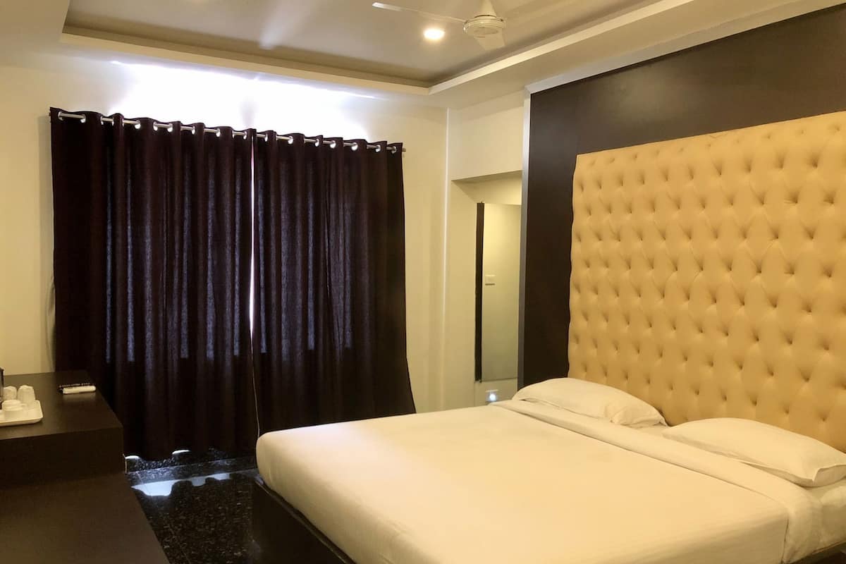 A hotel room with a bed, dark curtains, a bedside table with a remote control, and a ceiling fan.