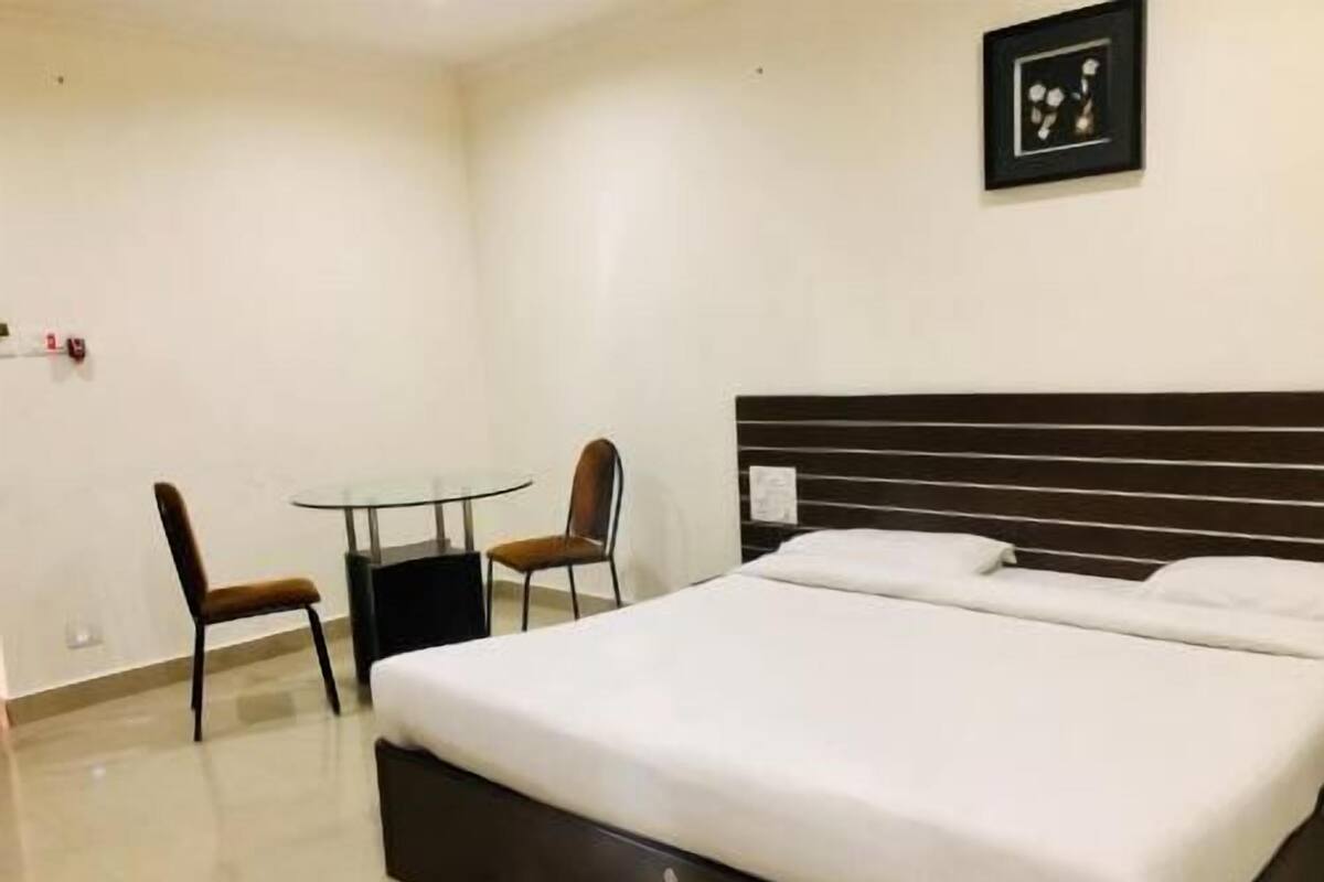 A hotel room with a bed, a small table, two chairs, and a framed picture on the wall.