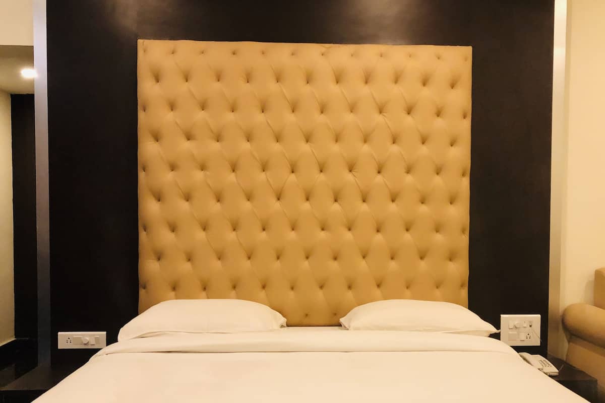 A large bed with a tufted headboard, white bedding, and a plain wall.