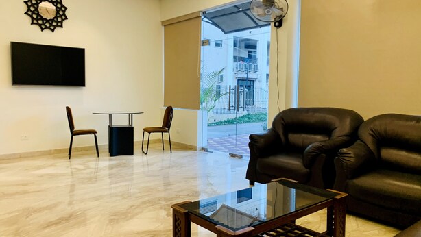 Un vaste espace de vie comprenant une table basse en verre, un canapé en cuir et un téléviseur fixé au mur.