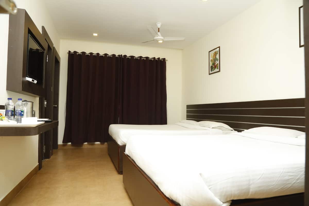 A hotel room with a bed, a TV mounted on the wall, a desk with a chair, and a window with curtains.