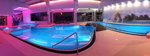 Una piscina interior moderna amb una paret de vidre, una zona d'estar a la vora de la piscina i un mural d'un paisatge natural.