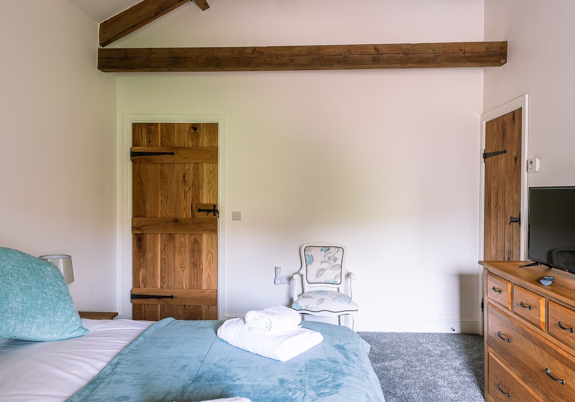 A bedroom with a wooden wardrobe, a chair, a dresser, and a bed with a blue blanket.