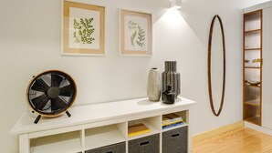 A modern room with a white console table, two framed botanical prints, a fan, and a wooden shelf unit. - Bright and designed apartment with Juliet balcony (Porto)