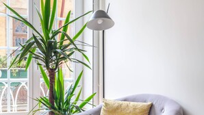 A modern living room with a grey armchair, a wooden side table, a floor lamp, and a large green plant. - Bright and designed apartment with Juliet balcony (Porto)