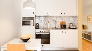 A compact kitchen with white cabinets, a marble backsplash, a microwave, a kettle, a toaster, and a wooden bowl on the table. - Bright and designed apartment with Juliet balcony (Porto)