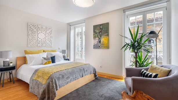 A modern bedroom with a large bed, a grey sofa, a wooden coffee table, and a large window with a view of the outside. - Bright and designed apartment with Juliet balcony (Porto)