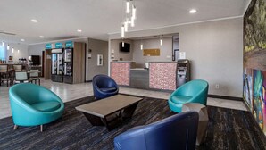 A modern lobby with teal chairs, a reception desk, a vending machine, and a coffee machine. - Clarion Pointe Sulphur - Lake Charles (Sulphur)