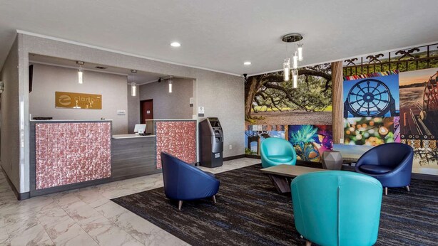 A hotel reception area with a marble floor, a reception desk, a self-service kiosk, and a seating area with modern chairs. - Clarion Pointe Sulphur - Lake Charles (Sulphur)