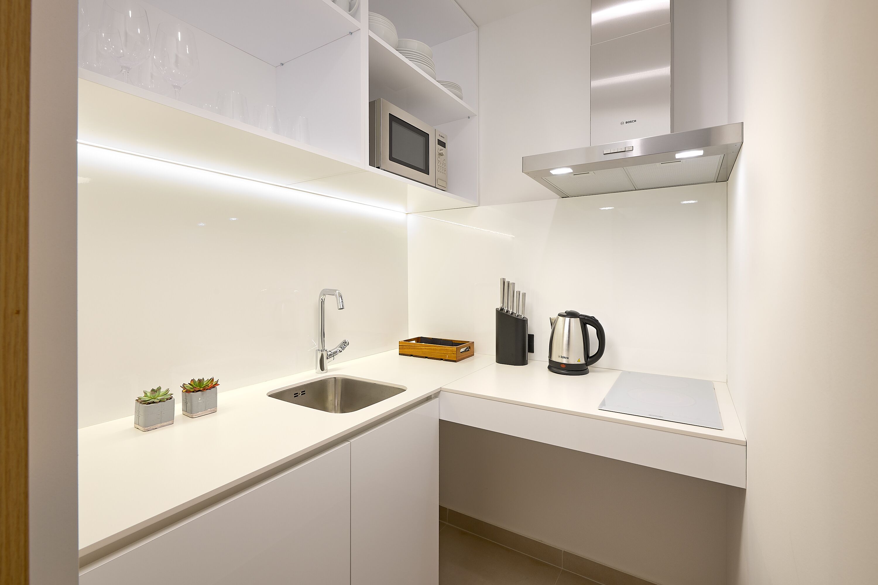 Una cocina moderna con armarios blancos, un lavamanos de acero inoxidable, un microondas Bosch y una tetera sobre la encimera.