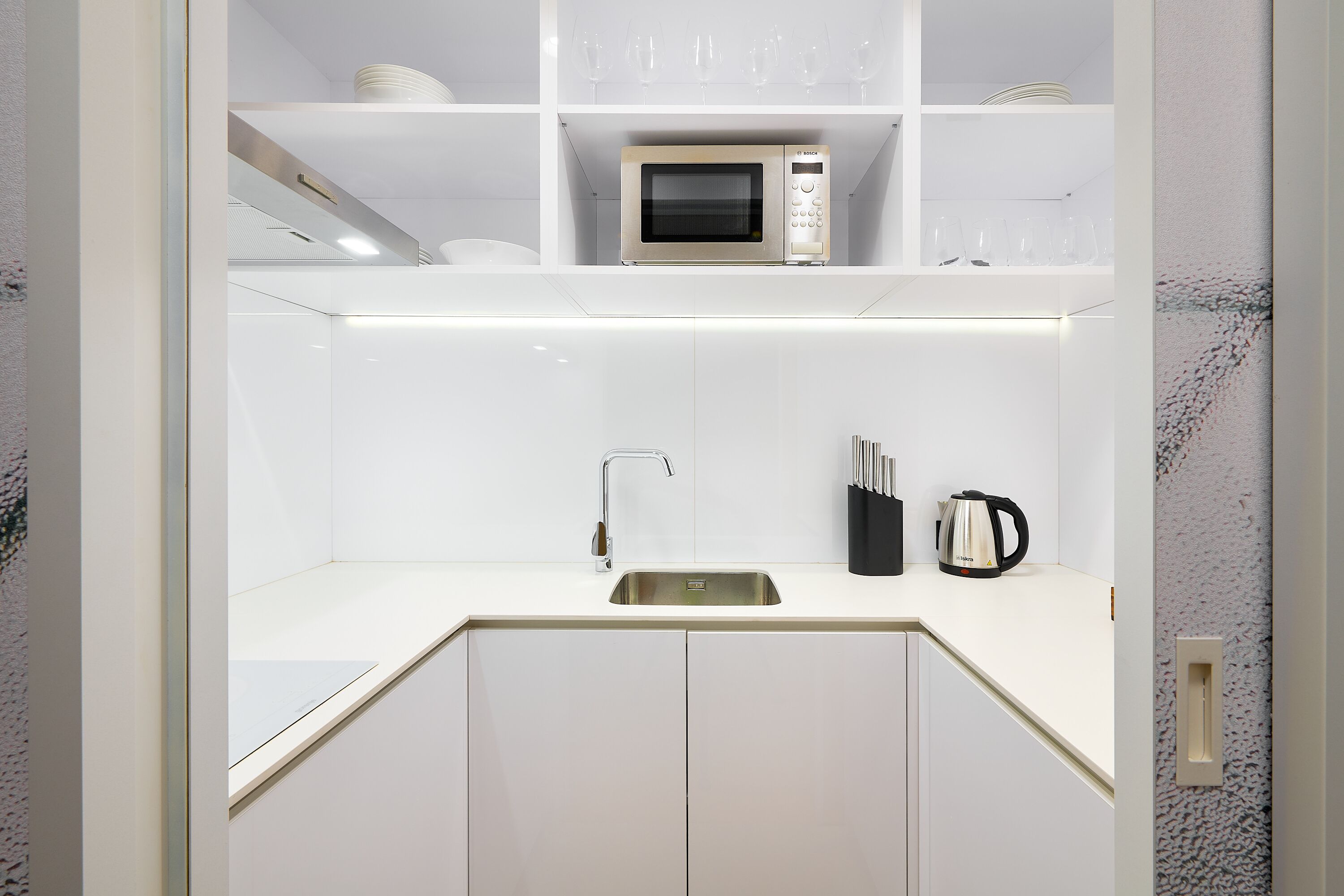 Een moderne keuken met witte kasten, een roestvrijstalen spoelbak, een magnetron en een koffiezetapparaat.