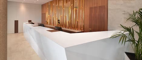 Un moderno mostrador de recepción con superficie blanca, paneles de madera y una planta en maceta.