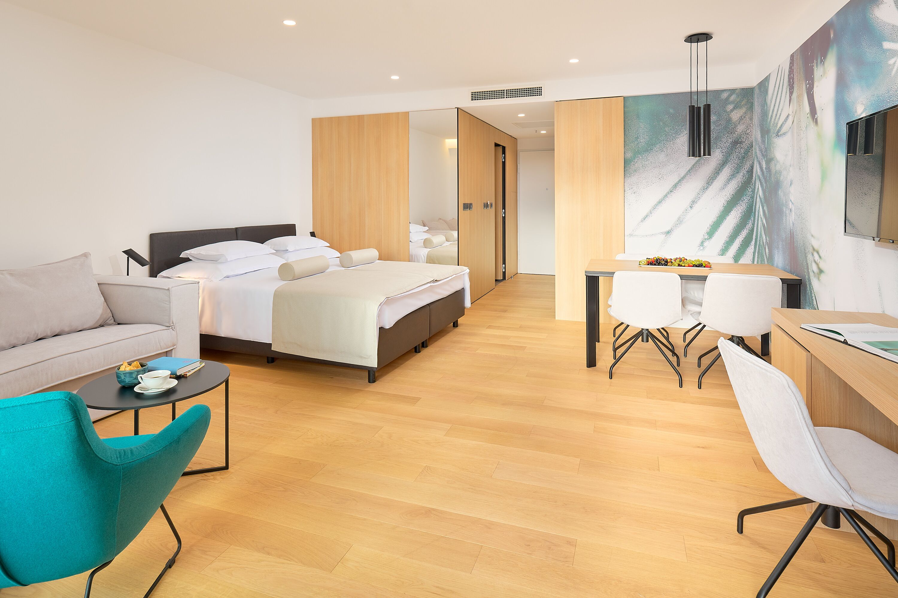 Een moderne hotelkamer met een bed, een slaapbank, een bureau met stoelen en een eettafel.