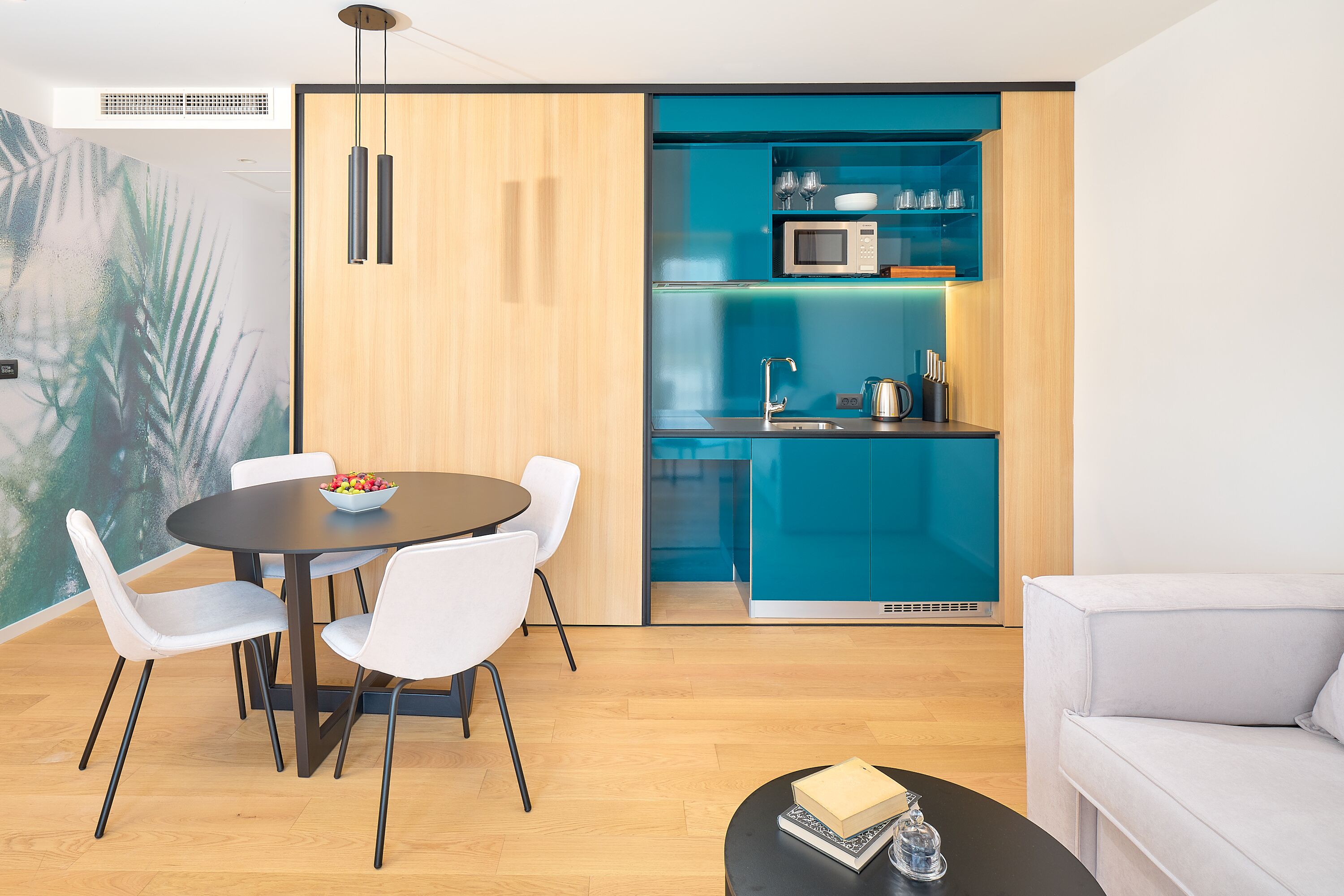 A modern kitchen with a microwave, sink, and blue cabinetry. There is a dining area with a round table and white chairs.