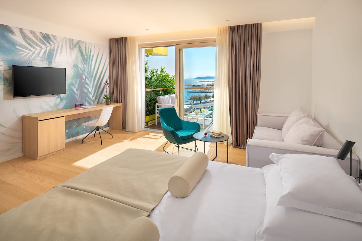 Ein Hotelzimmer mit Bett, Schreibtisch, Stuhl, Fernseher und Meerblick.