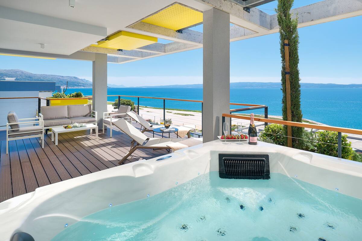 Eine Terrasse mit Whirlpool, Liegestühlen und einem Tisch mit einer Champagnerflasche.