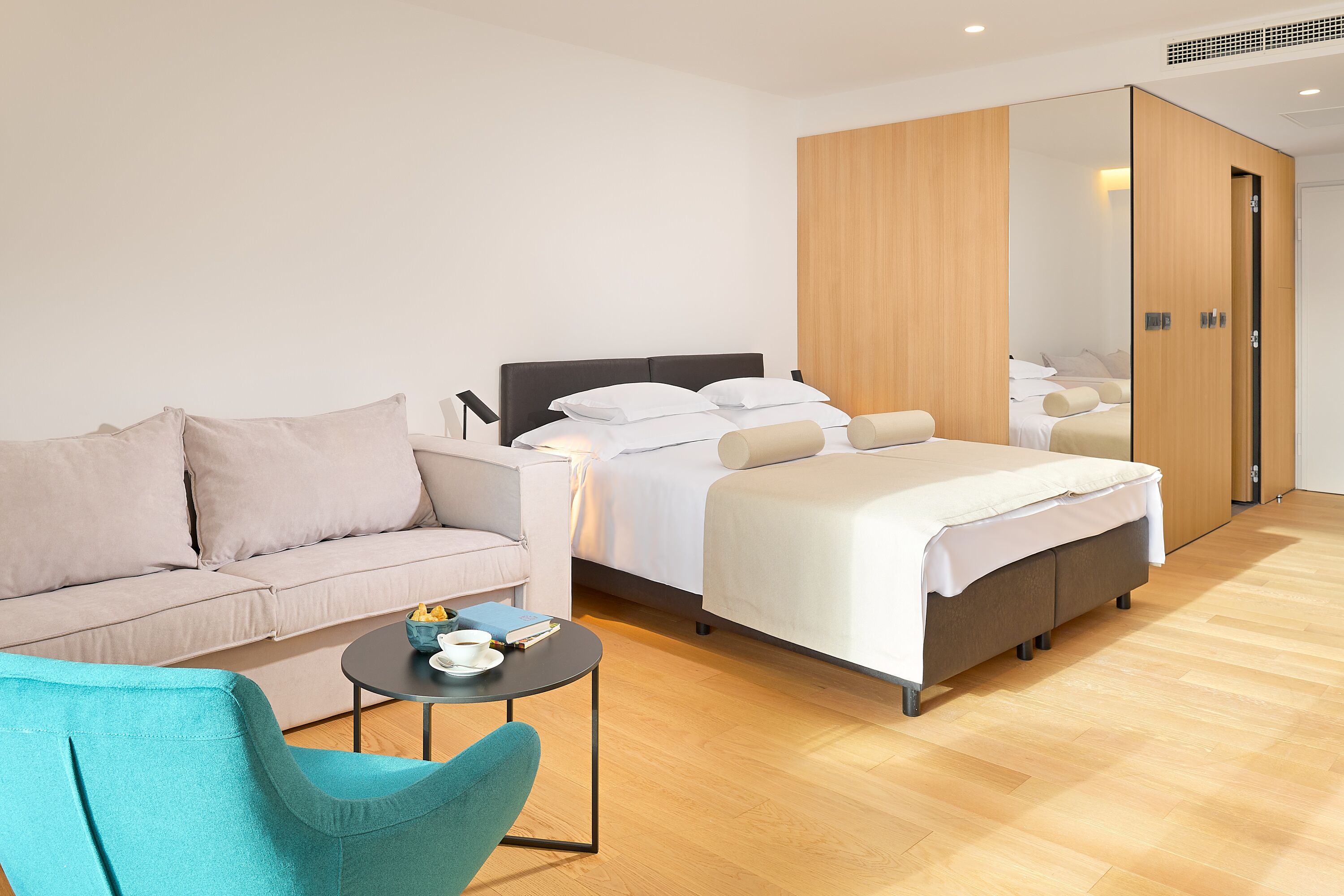 A modern hotel room with a sofa, a bed, a small table, and a mirror.