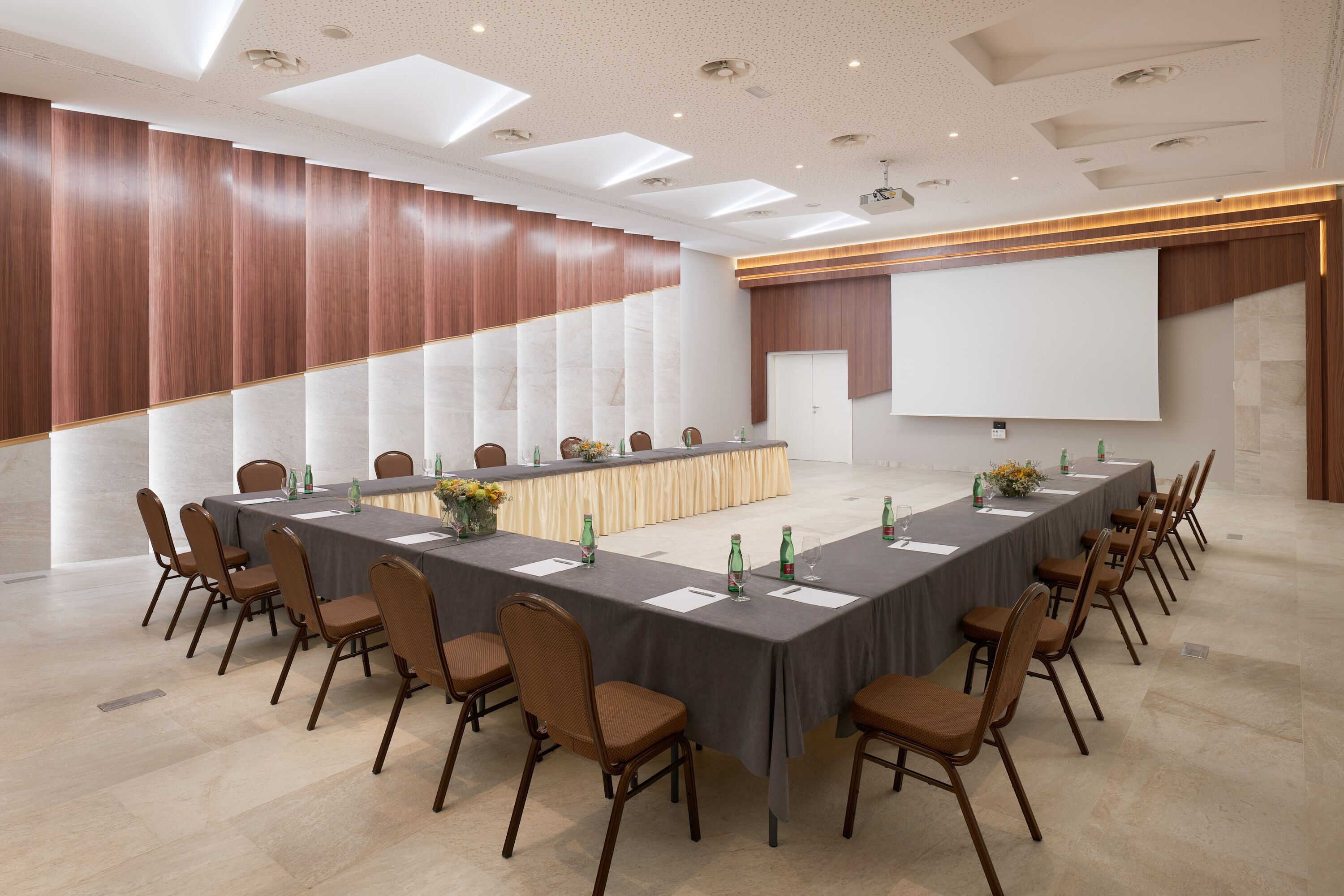 A conference room with a long table, chairs, a podium, and a large screen.