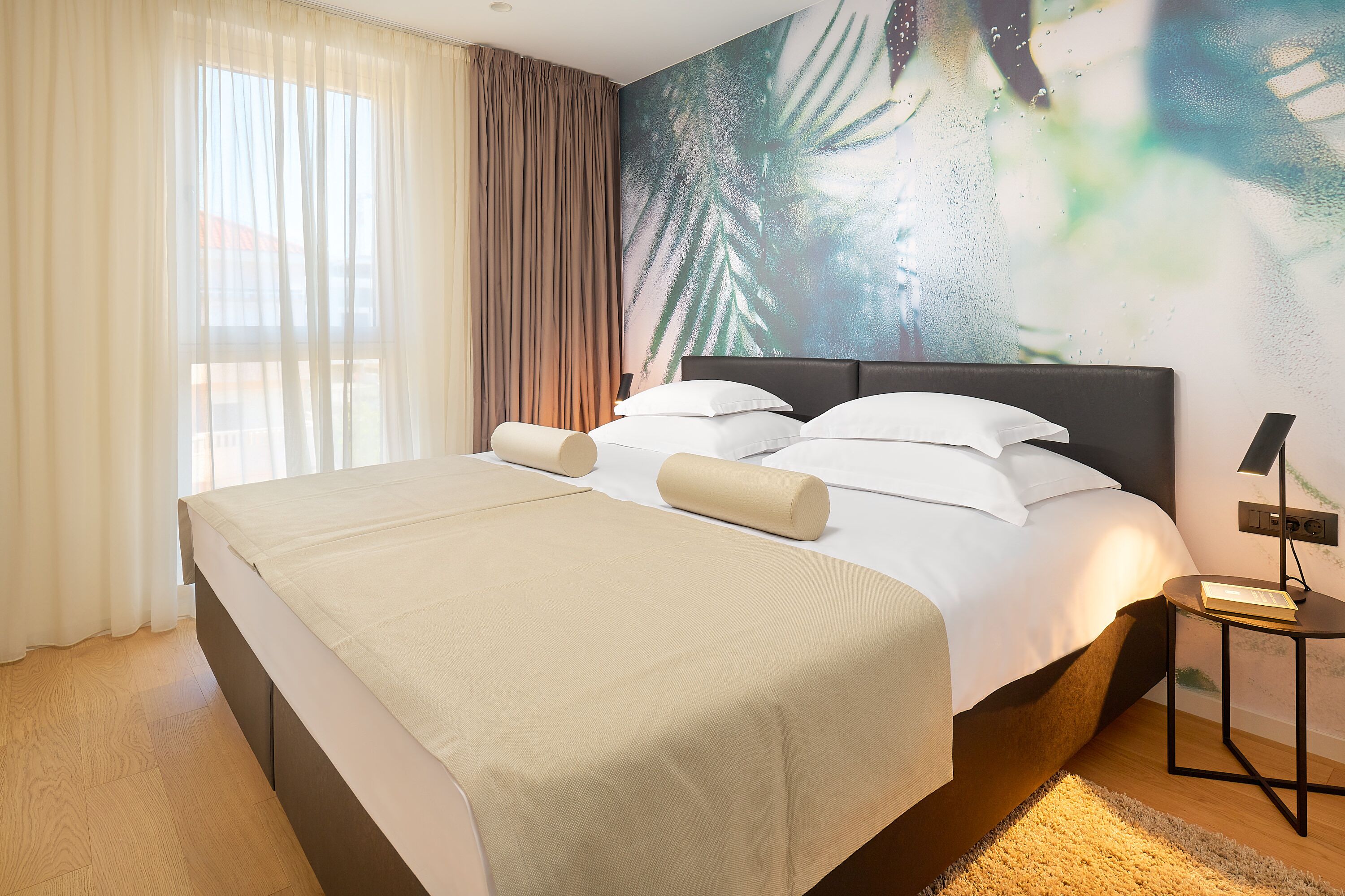 A hotel room with a large bed, a nightstand, and a wall mural.
