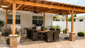 An outdoor patio with a pergola, dining table, chairs, and potted plants.