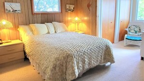 Een slaapkamer met een groot bed, houten paneelwanden, twee bedlampen, een raam met uitzicht en een deur naar een andere kamer.