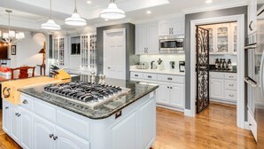A modern kitchen with white cabinetry, a central island with a stove, and pendant lighting. - Awesome Hilltop Views, Pool, Vineyards, Olive Trees, 5 mins to Healdsburg (Healdsburg)