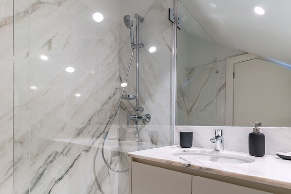 A modern bathroom with a marble wall, a shower, a sink, and a mirror.
