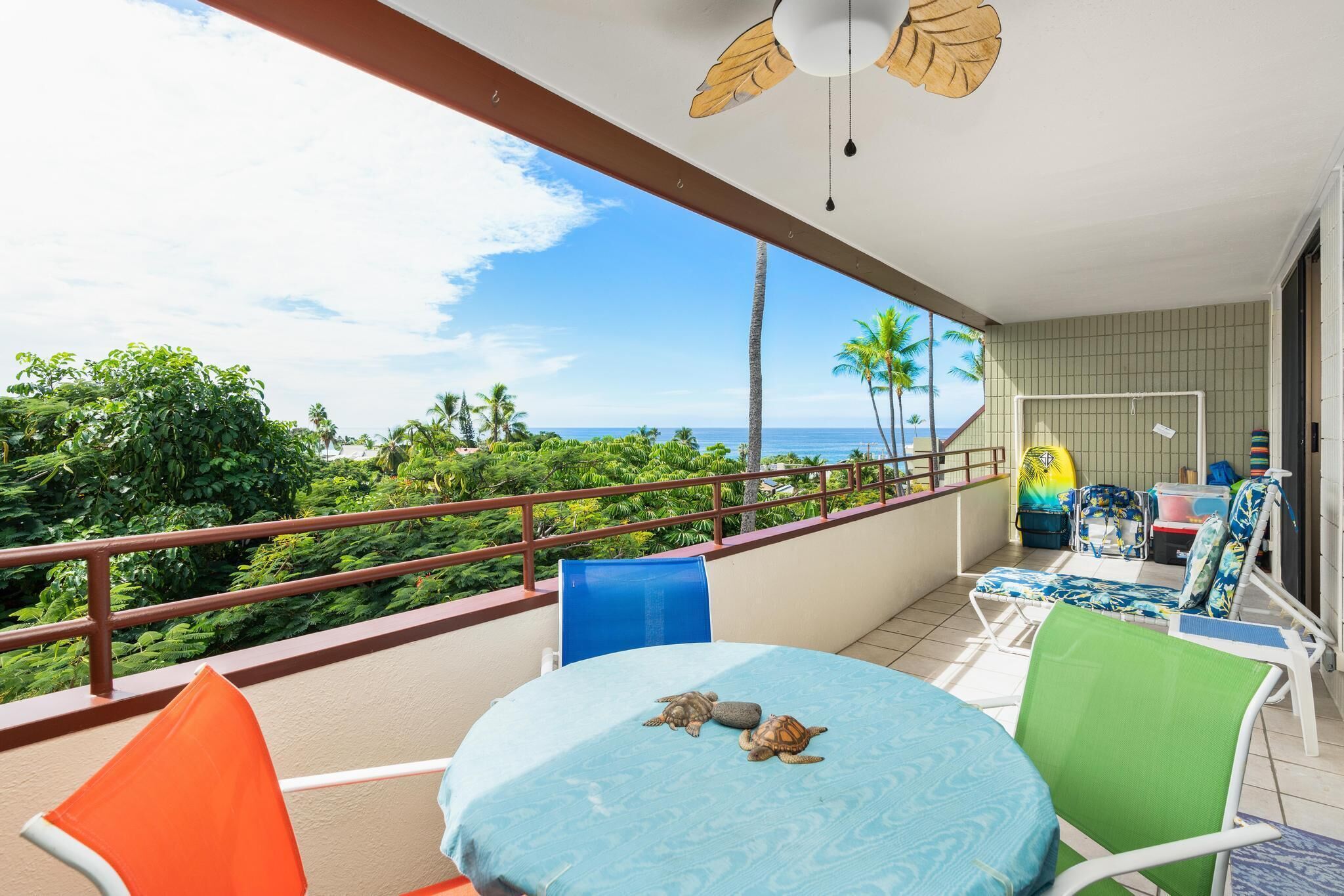 A balcony with a table, chairs, and a view of the ocean and palm trees.