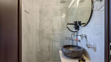 A modern bathroom with a large mirror, a round sink, and a shower.