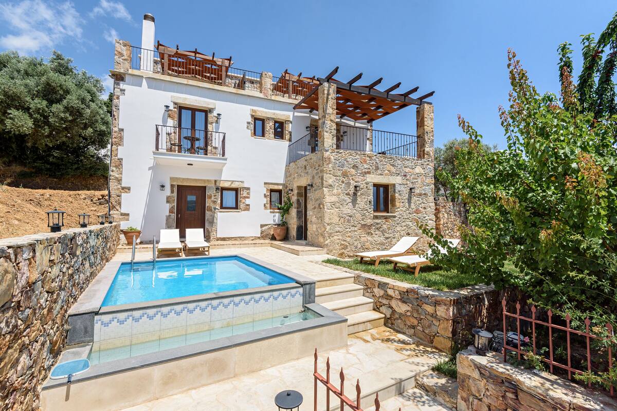 Un edificio de dos pisos con piscina, paredes de piedra y mobiliario exterior.
