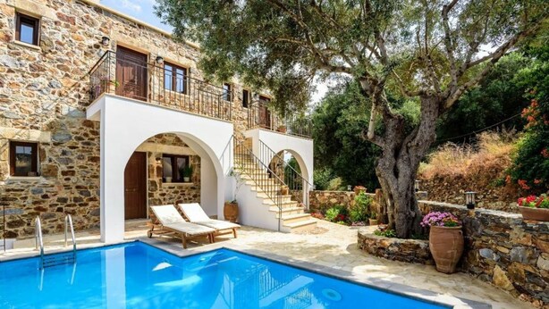 Un edificio de piedra con piscina, mobiliario exterior y una escalera que conduce a un balcón.