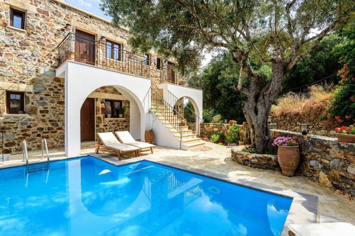 Un edificio de piedra con piscina, mobiliario exterior y una escalera que conduce a un balcón.