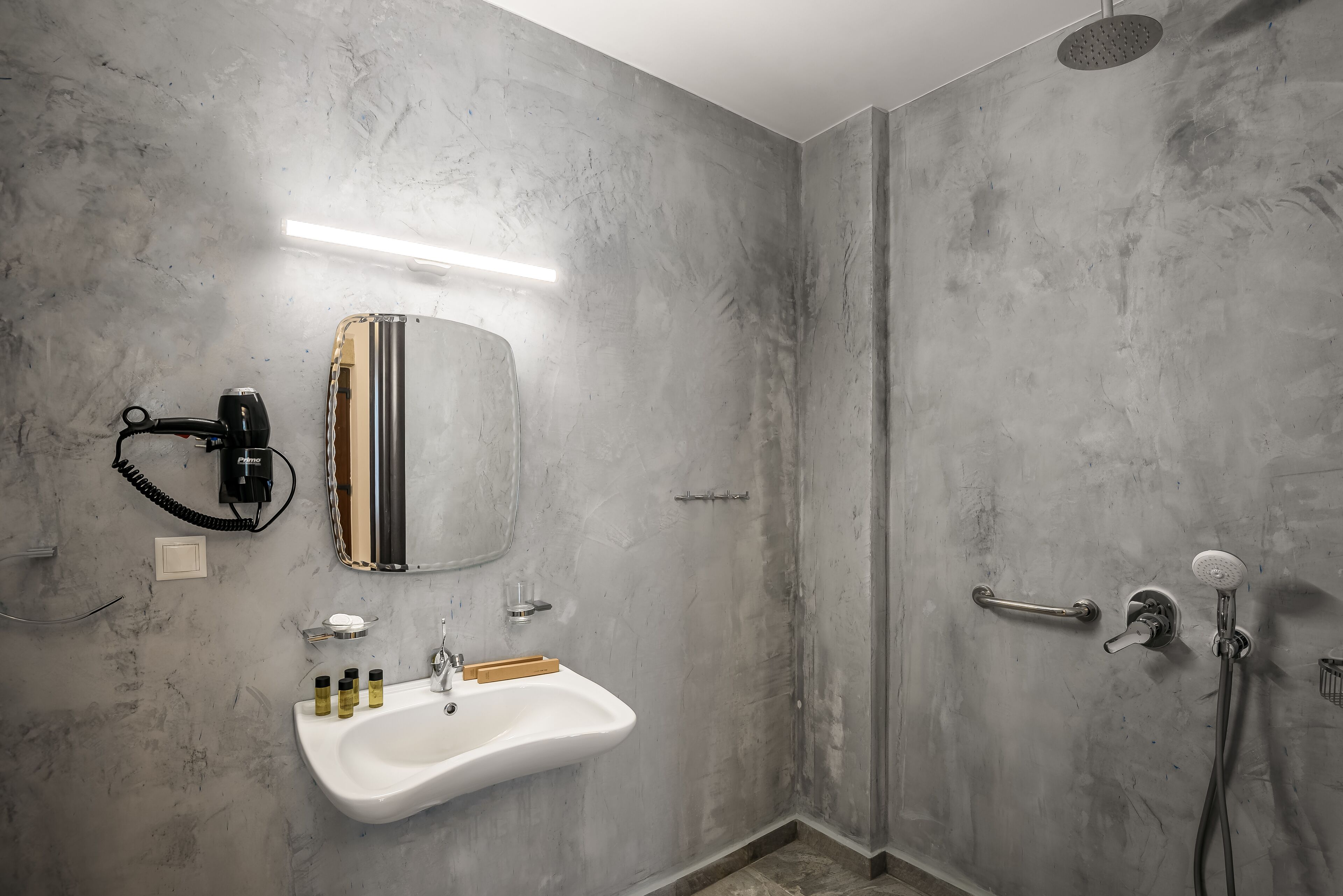 Une salle de bain dotée d’un grand miroir, d’un lavabo avec des articles de toilette, d’une douchette et d’un porte-serviettes.