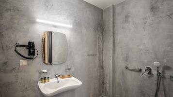Une salle de bain dotée d’un grand miroir, d’un lavabo avec des articles de toilette, d’une douchette et d’un porte-serviettes.