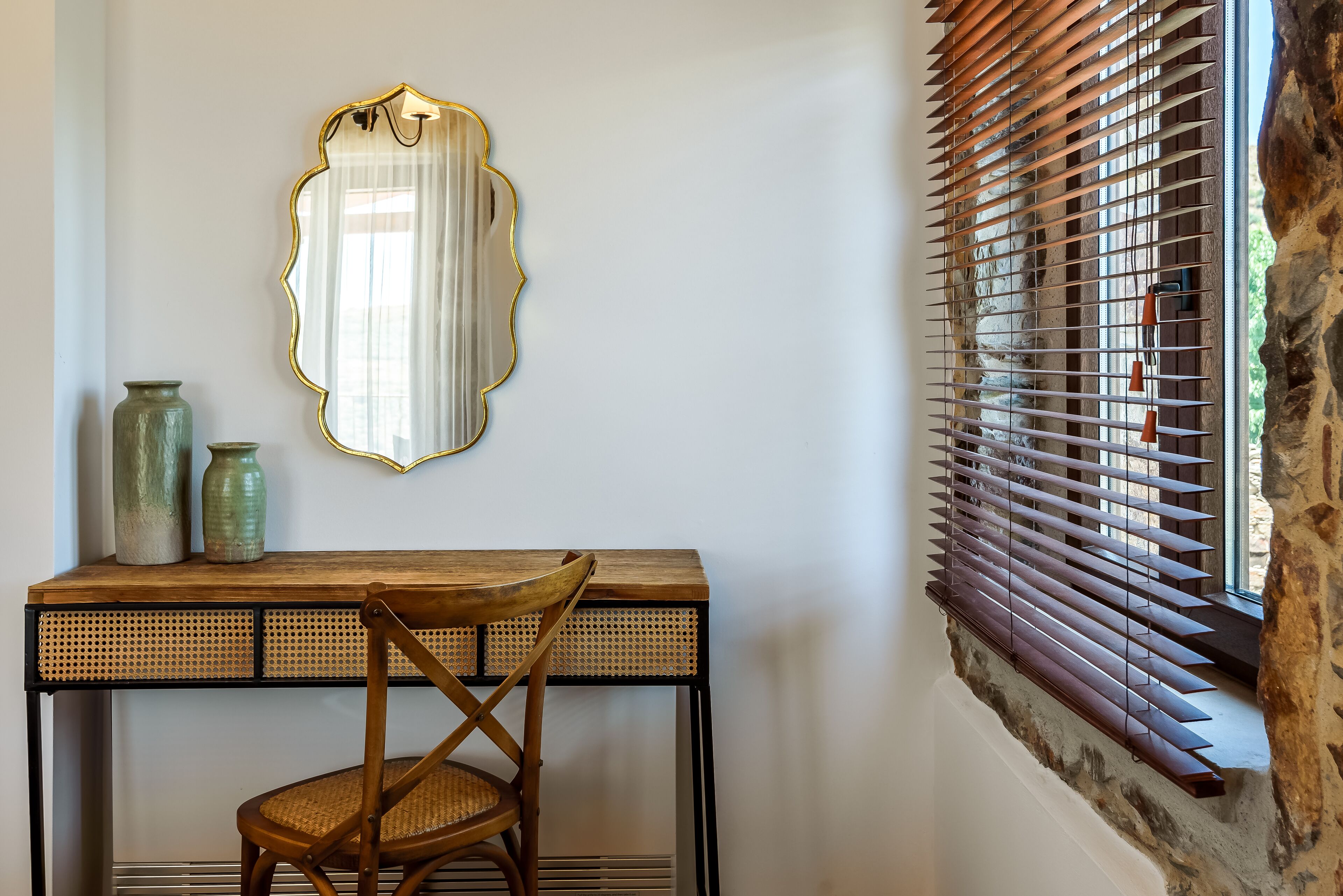 A room with a wooden desk, a chair, a mirror, and a window with wooden blinds.